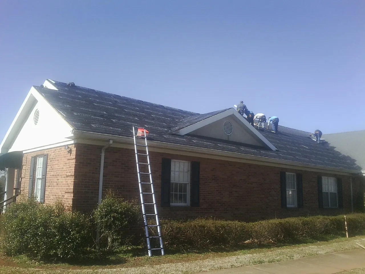 Crew tearing shingles off a brick ranch roof with a ladder set — Emergency Roof Repair work by our crew in Wheeler