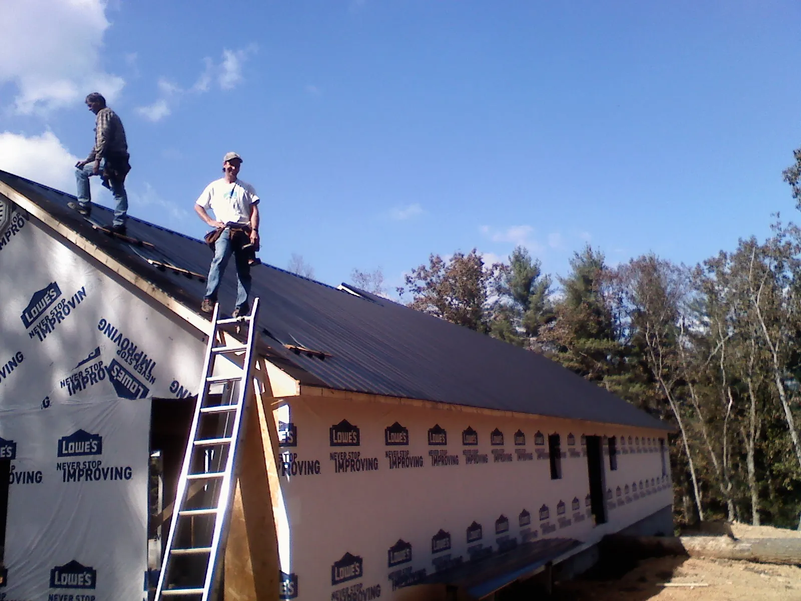 Two roofers standing on a long dark metal roof over a wrapped building in Wheeler